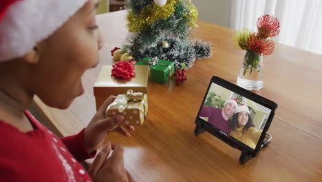 mujer afroamericana con sombrero de santa usando tableta para una videollamada de navidad con una pareja en la pantalla