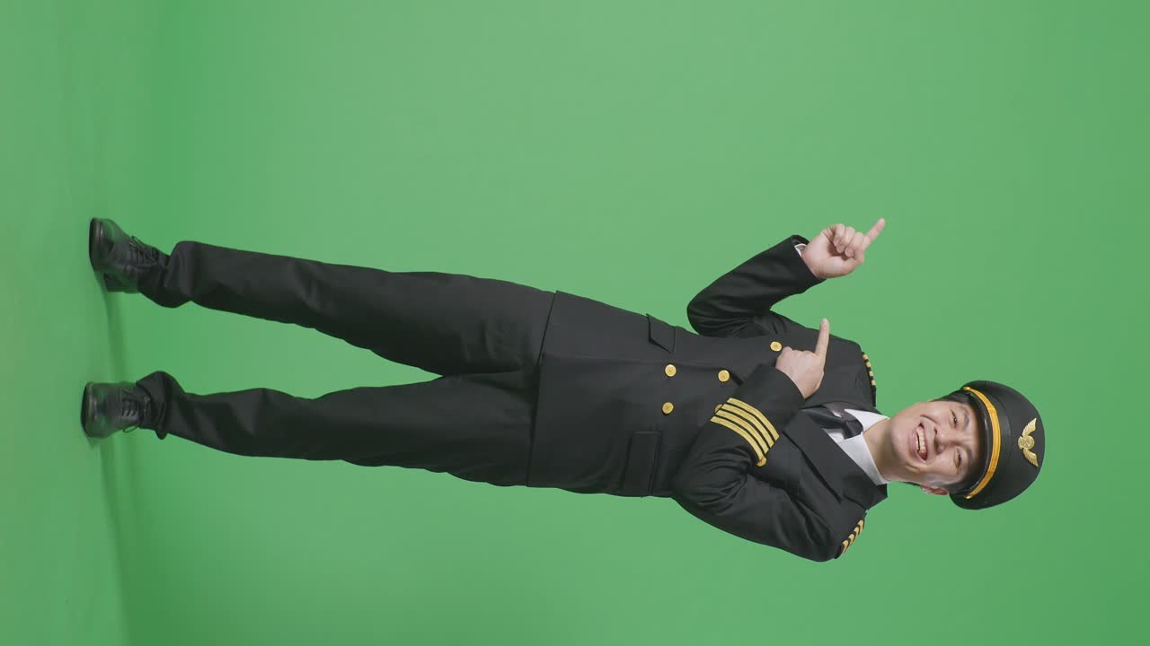 полное тело азиатского человека пилот улыбается и указывает на сторону, стоя в зеленом экране фоновой студии