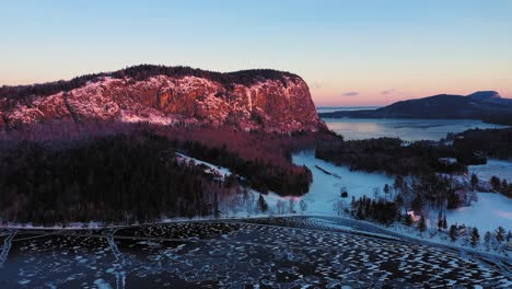 aerial pull back away from the peak of a cliff faced mountain during a winter sunrise