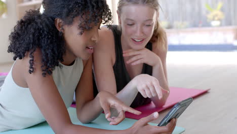 happy diverse women lying on yoga mats and using smartphone, slow motion