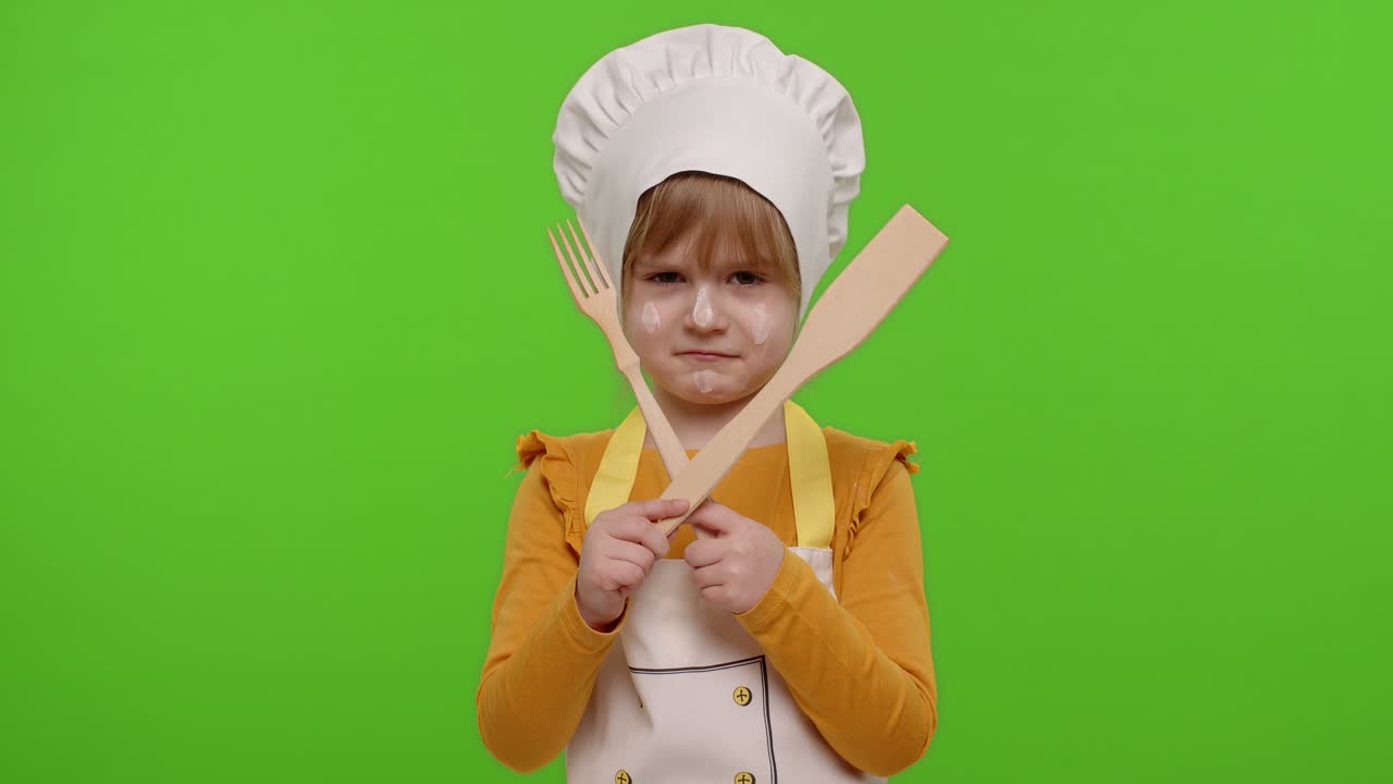 Bambina vestita da cuoca chef con forchetta e spatola, che mostra un simbolo di rifiuto, disaccordo.