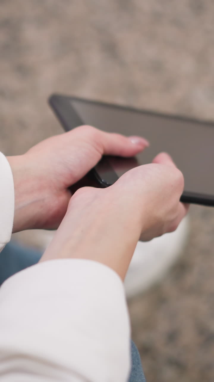 화면에 반사되는 태블릿을 만들기 위해 그라나이트 바닥에 앉아있는 동안  팔에 손을 고 손을 부드럽게 흔들고 있습니다.