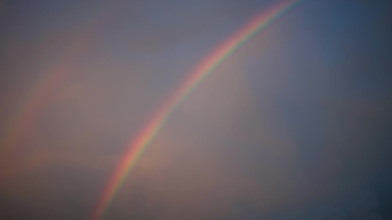Håndholdt video fanger en slående regnbue, der buer gennem mørke regnskyer i USA. Blødt, stemningsfuldt aftenlys og bevægelige teksturer skaber et fredfyldt, atmosfærisk vejrbillede.