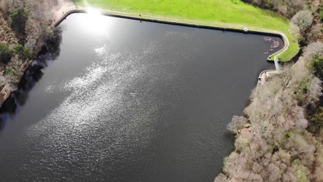 Aerial-Flying-Over-Squabmoor-Reservoir-With-Sunlight-Being-Reflected-Off-Surface