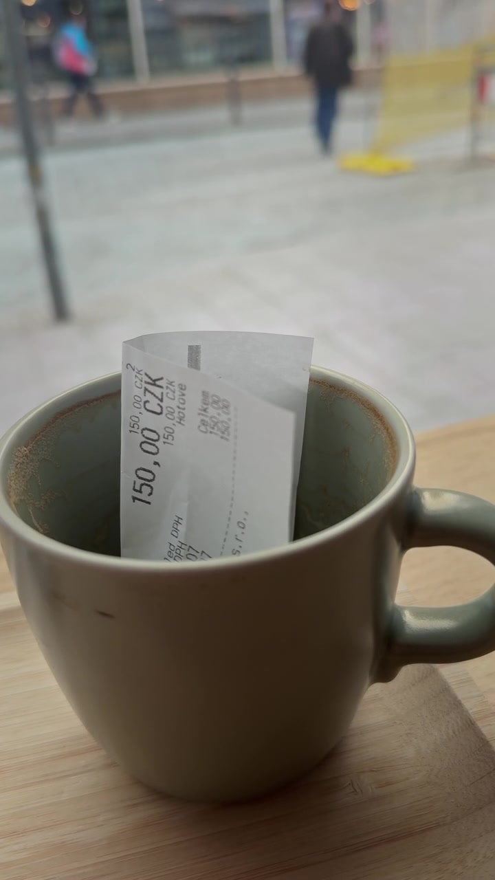 Primer plano de un recibo de café pagado descansando dentro de una taza de café vacía con la suave vida de la ciudad más allá de la ventana, simbolizando rutinas diarias, hábitos de gasto y momentos fugaces.