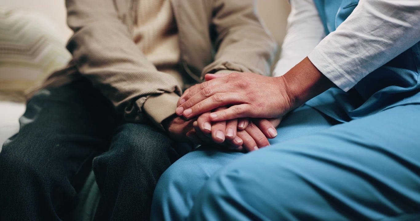 Infermiera che conforta un paziente anziano tenendogli le mani
