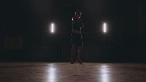 Training-a-beautiful-female-boxer-doing-punches-in-a-dark-room.-Steadicam-shot.-Preparation-for-self-defense-and-fight-in-the-ring