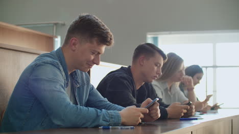 two friends are sitting in a large classroom with students and showing each other funny videos from the boarding school. have fun and have fun at the university