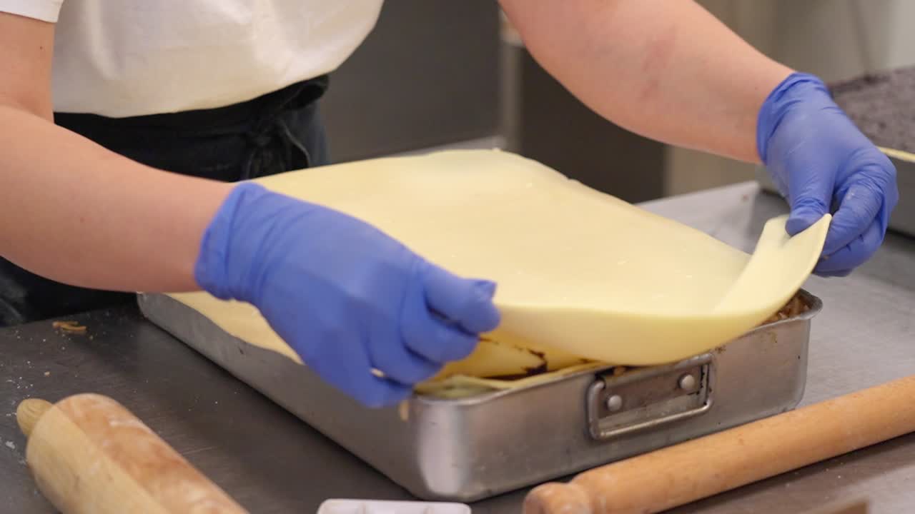 Dough being rolled over flódni layers in a tray