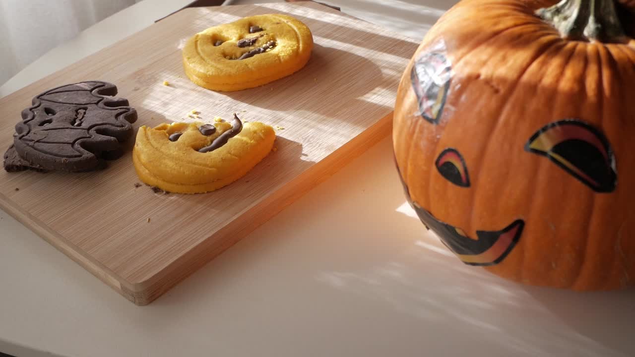 Close-up of pumpkin-shaped cookies beside a Halloween pumpkin decoration on wooden board under warm daylight