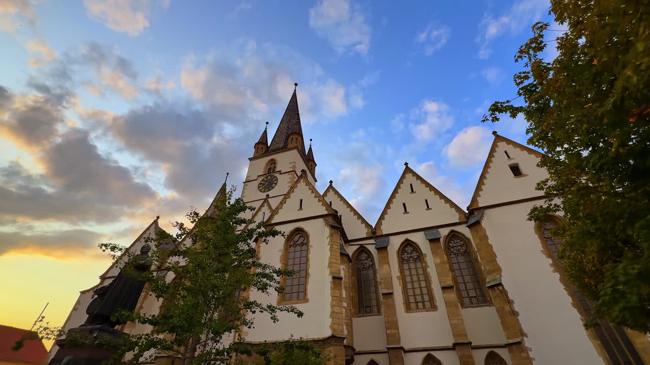 Lively daytime at Sibiu main square. Church tower and baroque buildings surround cobblestone paths filled with tourists