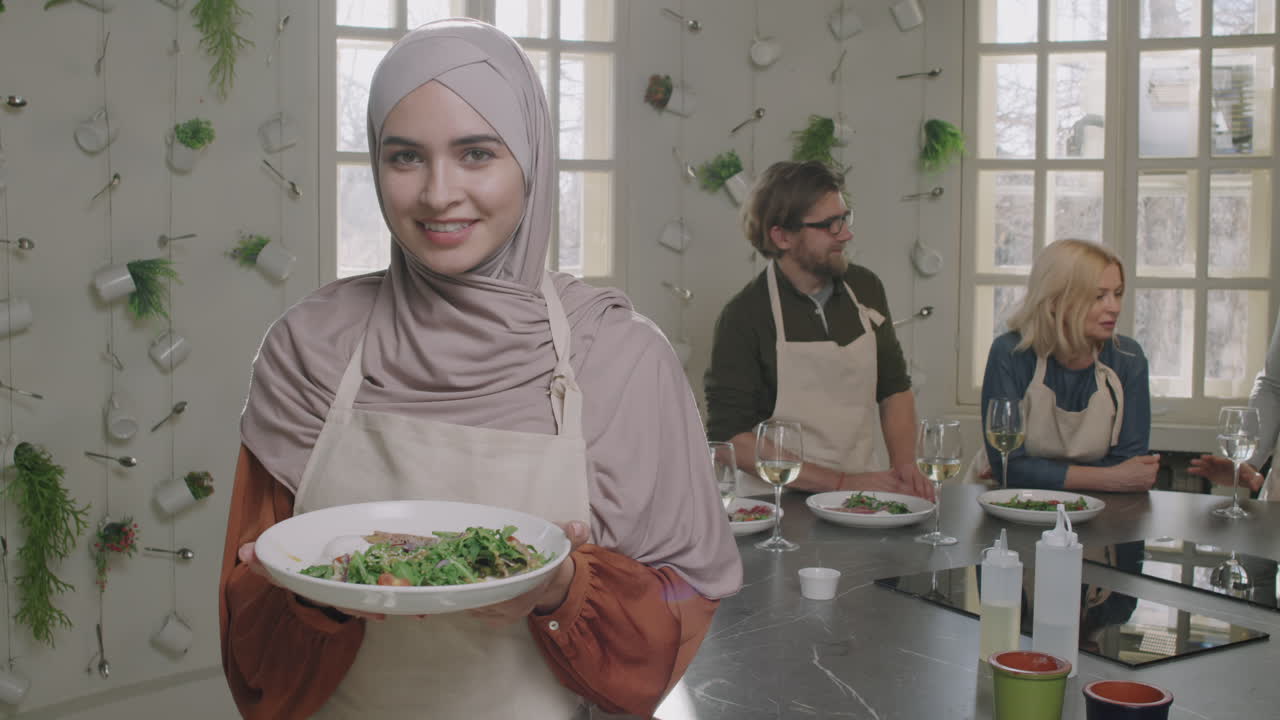 A woman in a hijab holding a plate of salad during a cooking class