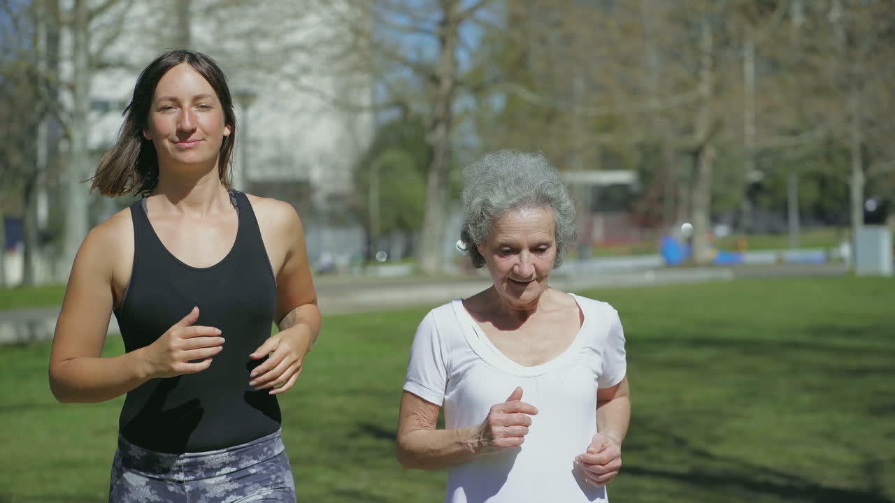 Front view of two women jogging in park, talking and smiling