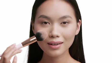 young asian woman applying makeup with a brush