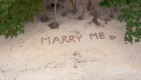 tropical beach marriage proposal with 'marry me' written in sand
