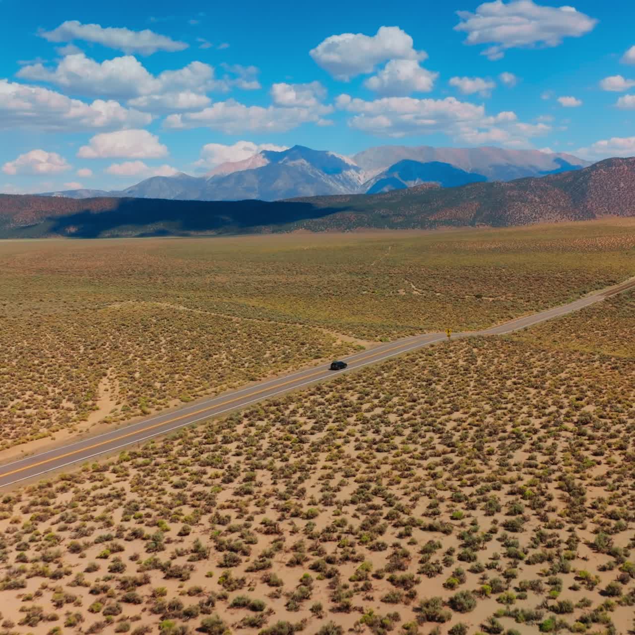 Motorway along the desert limited by mountain range. Soft cumulus clouds throwing shadows on the rocks. Aerial view