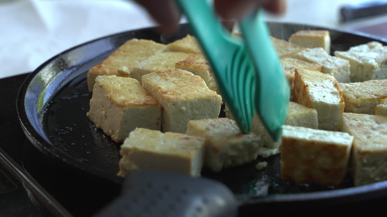 Tofu extra-fermo in cottura e girato su una padella di ghisa, ingredienti speciali per cucinare un pasto: due lattine di fagioli, riso, platano, avocado, cipolla rossa e coriandolo