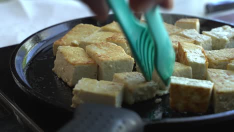 extra firm tofu being cooked and turned on a cast iron pan special ingredients to cook a meal two cans of beans rice plantain avocado red onion and cilantro