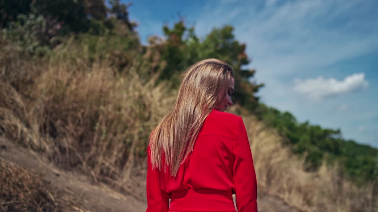 Sexy woman with long hair outdors. Backside view of a pretty woman in bright dress walking in nature. Slow motion.