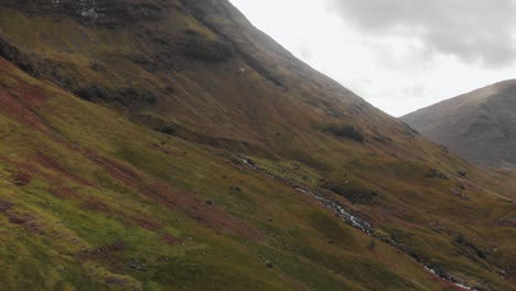 flying toward a stream making its way downhill along an epic landscape in the glencoe area of scotland