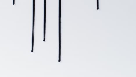 close up of black paint shapes on white background with copy space, slow motion