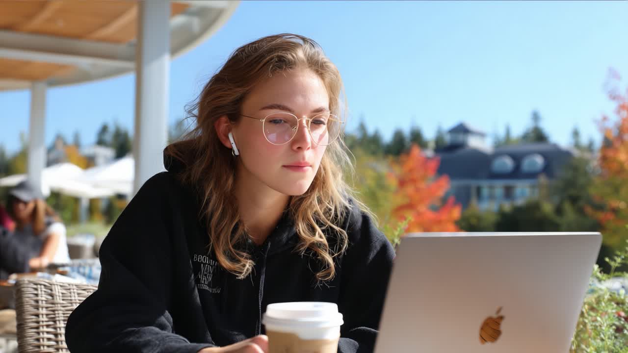 Fokuseret og kreativ: En ung kvinde nyder en kop kaffe, mens hun arbejder på en bærbar computer i smukke omgivelser med efterårsfarver i baggrunden