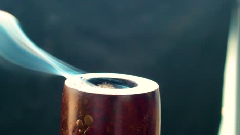 extreme-close-up-of-a-old-fashioned-pipe-top-part-only-that-vapour-a-thick-smoke-of-blue-colour-looking-like-a-spirit-essence-of-something-greater-wooden-build-black-back-drop-indoor-setup