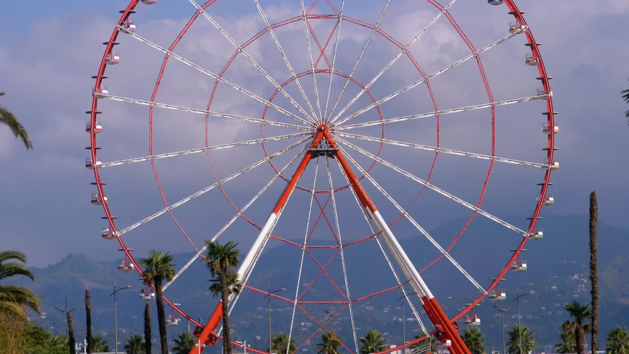 rueda gigante contra el cielo azul con nubes cerca de las palmeras en la ciudad turística, día soleado
