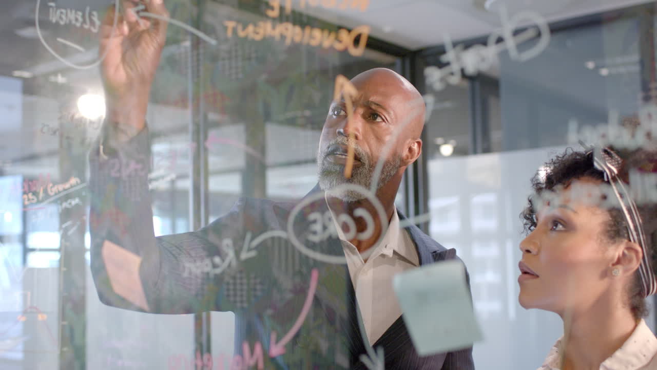 African american businessman writing on glass wall in office with copy space