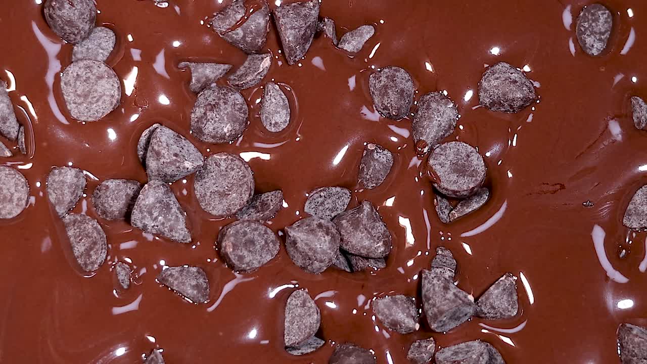 Close-up of chocolate chips gently landing on a smooth, glossy chocolate surface.