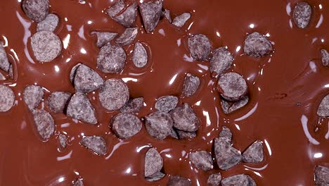 close-up of chocolate chips gently landing on a smooth, glossy chocolate surface.