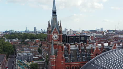 Beautiful-decorated-brick-clock-tower-as-part-of-old-brick-St-Pancras-train-station-building.-Modern-downtown-skyscrapers-in-background.-London,-UK