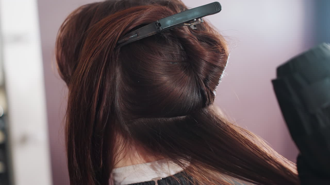 머리 섹션을 나누고 클립을 준비하는 백인 여성, 컬러리스트 또는 스타일리스트가 금속 클립으로 하단 패널을 분리하고, 장갑을 낀 손으로 머리카락을 고정하며, 미용실 스테이션이 보이고, 전문적인 준비에 집중하고 있어요.