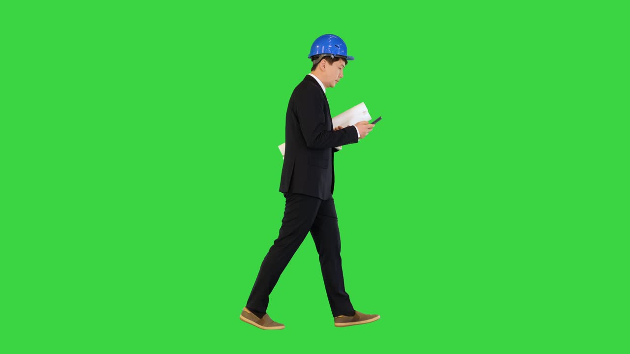 Architect man holding blueprints using smartphone and walking on a Green Screen, Chroma Key
