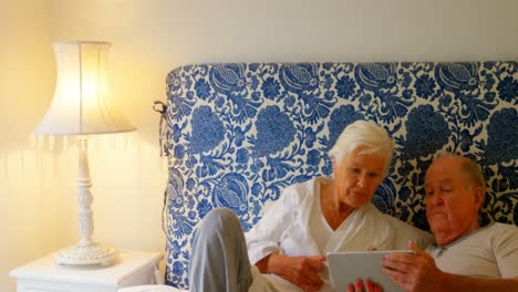 Vorderansicht-Eines-Kaukasischen-Seniorenpaares,-Das-über-Ein-Digitales-Tablet-Auf-Dem-Bett-In-Einem-Komfortablen-Zuhause-Diskutiert,-4K