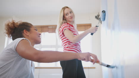 two women decorating room in new home painting wall together