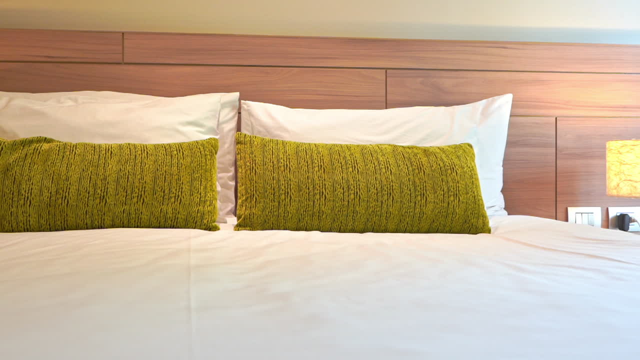panorámica lenta en una cama king size hecha dos juegos de almohadas blancas y verdes y una lámpara de noche en la habitación del hotel