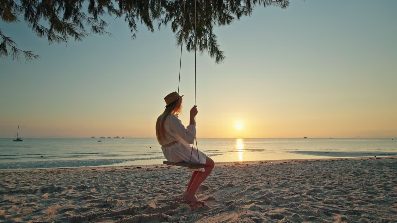 Donna su un'altalena sulla spiaggia al tramonto
