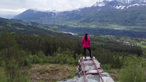 Antena-Moviéndose-Hacia-Atrás-Y-Revelando-A-Una-Mujer-Hermosa-De-Pie-En-El-Mirador-De-Voss-Noruega---Mina-De-Pizarra-De-Nordheim-Mirando-Hacia-El-Lago-Lonavatnet-Y-El-Centro-De-Voss