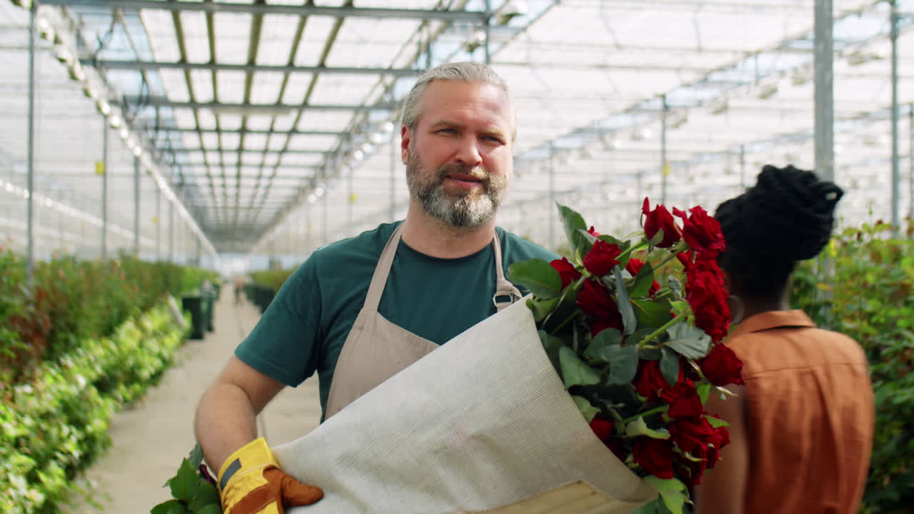hombre de mediana edad caminando con rosas en el invernadero de flores