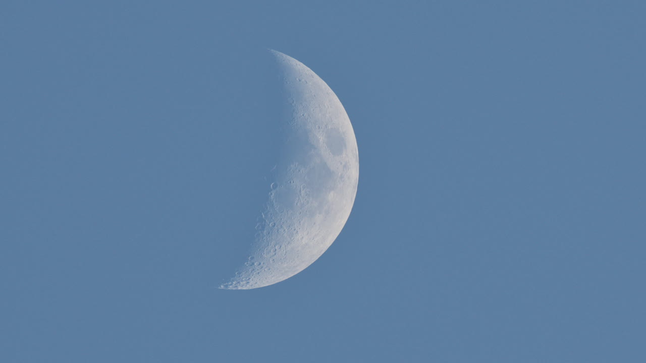 Crescent moon rising in blue sky during daytime, isolated against a clear sky backdrop background with space for text
