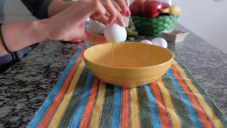 Woman-hands-breaking-the-shell-of-an-egg-and-pouring-it-into-a-bowl