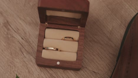 close up of two gold wedding rings in a wooden ring box on a wooden surface during wedding prep