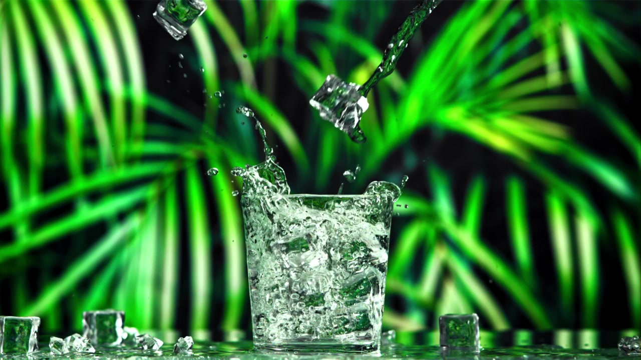 Acqua limpida versata in un bicchiere con cubetti di ghiaccio e sfondo tropicale verde