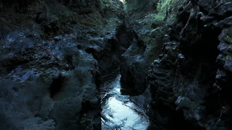 Aerial-flying-through-tight-canyon-with-rocky-walls-and-water-flowing-gently