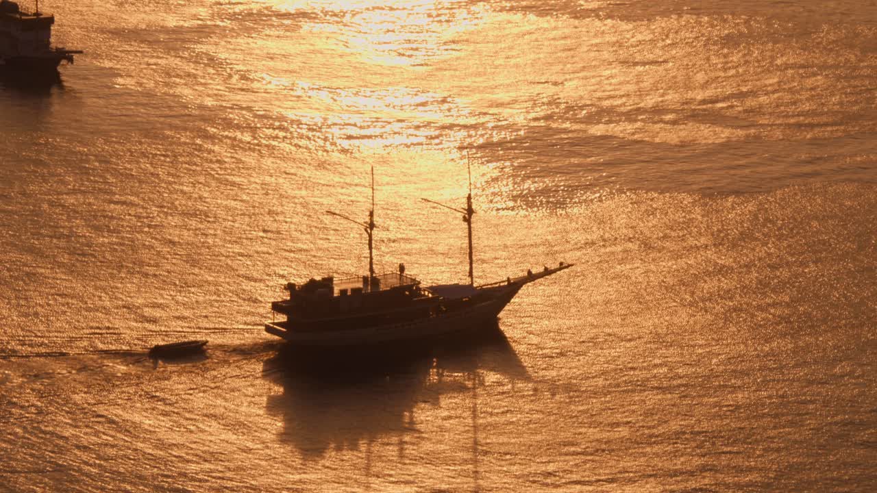 Aerial view of a sailboat gracefully sailing across golden waters against a backdrop of a setting sun