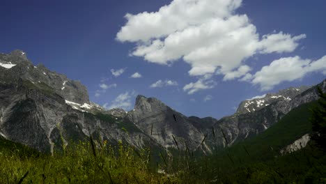 Friedliche-Alpine-Landschaft-Der-Grünen-Wiese-Mit-Hohen-Bergen,-Blauem-Himmel-Und-Wolkenhintergrund