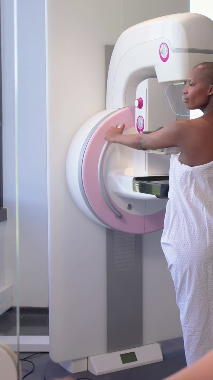 Video verticale: Tecnico che tocca i controlli, guidando una donna in camice bianco all'unità di mammografia per l'esame.