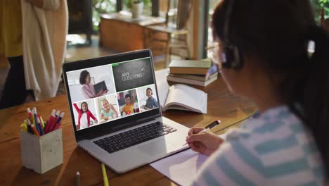 Schoolgirl-using-laptop-for-online-lesson-at-home,-with-diverse-teacher-and-class-on-screen