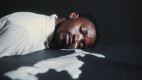 man resting head on dark floor and crying with white paint as tears